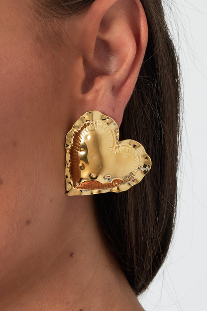 Close-up of a model wearing one gold-tone puffy heart shaped stud earring showing its size and shine