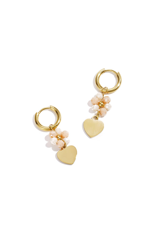 Pair of gold-tone hoop earrings with light peach faceted beads and dangling gold heart charms on white background