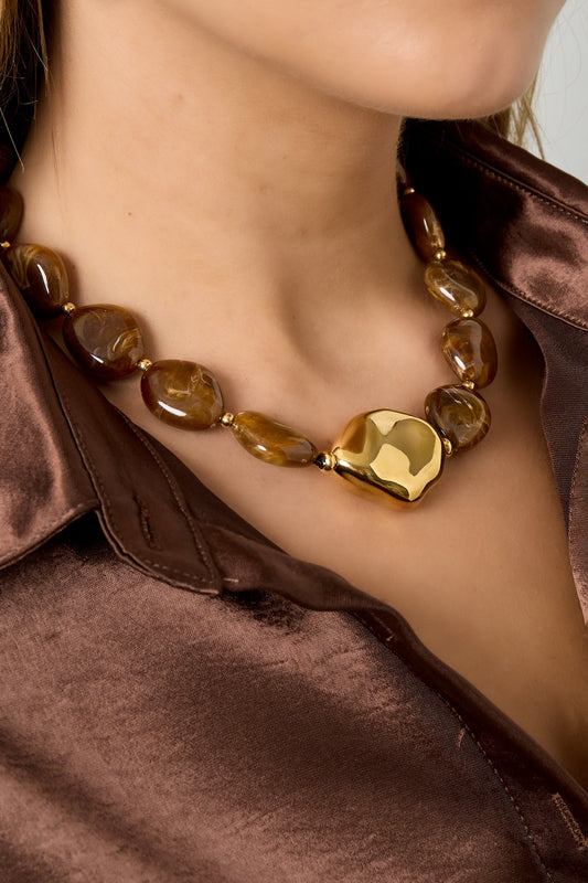 Model wearing warm brown acrylic beaded necklace with shiny gold centerpiece paired with silky brown shirt