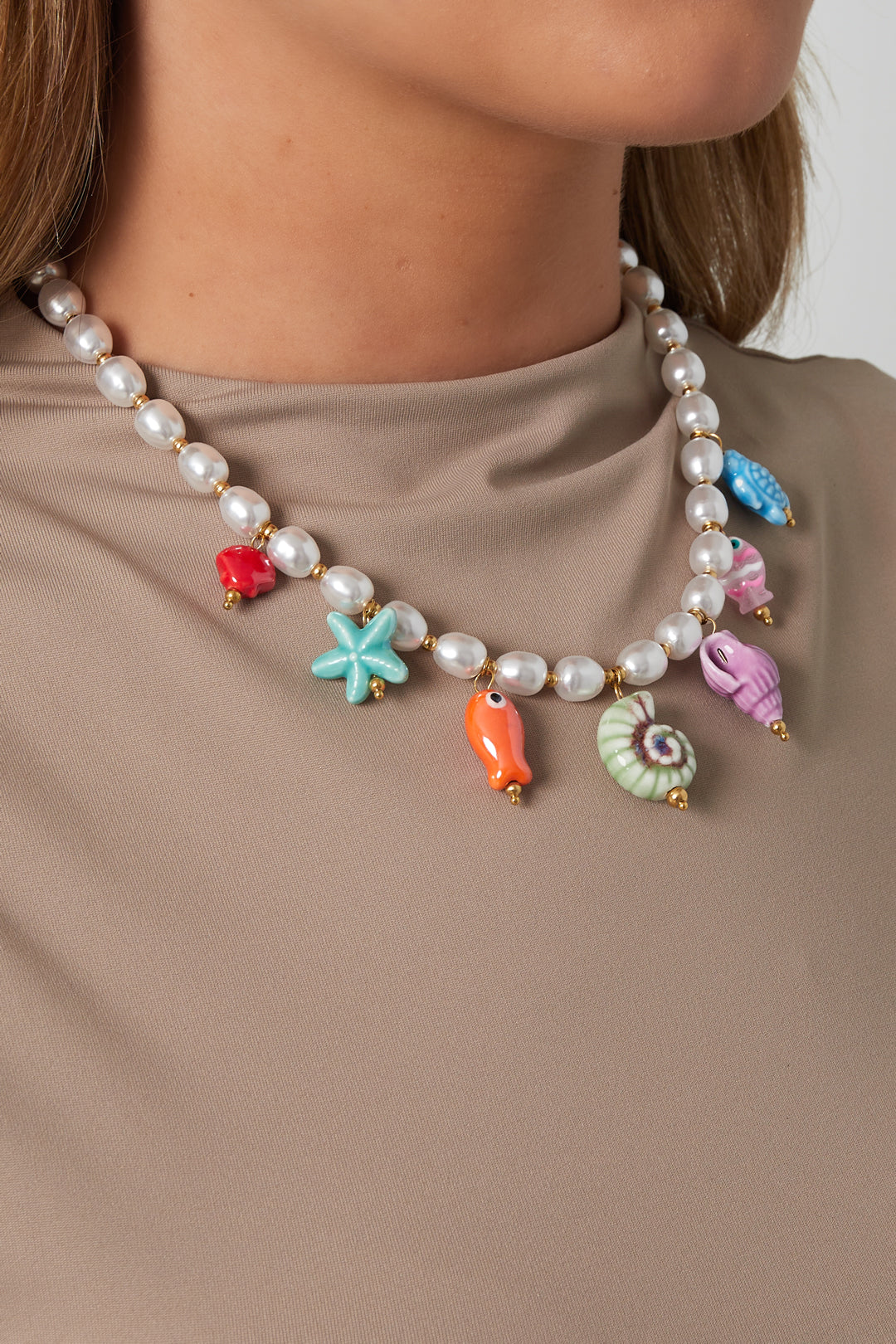 Woman wearing a playful pearl necklace with vibrant ceramic sea life charms over a beige top, showcasing youthful and boutique style.