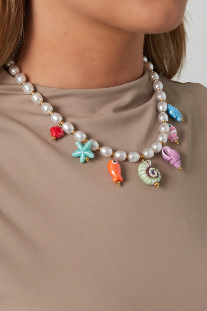 Woman wearing a playful pearl necklace with vibrant ceramic sea life charms over a beige top, showcasing youthful and boutique style.