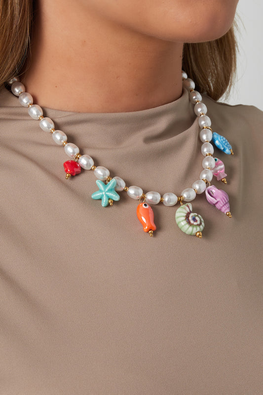 Woman wearing a playful pearl necklace with vibrant ceramic sea life charms over a beige top, showcasing youthful and boutique style.