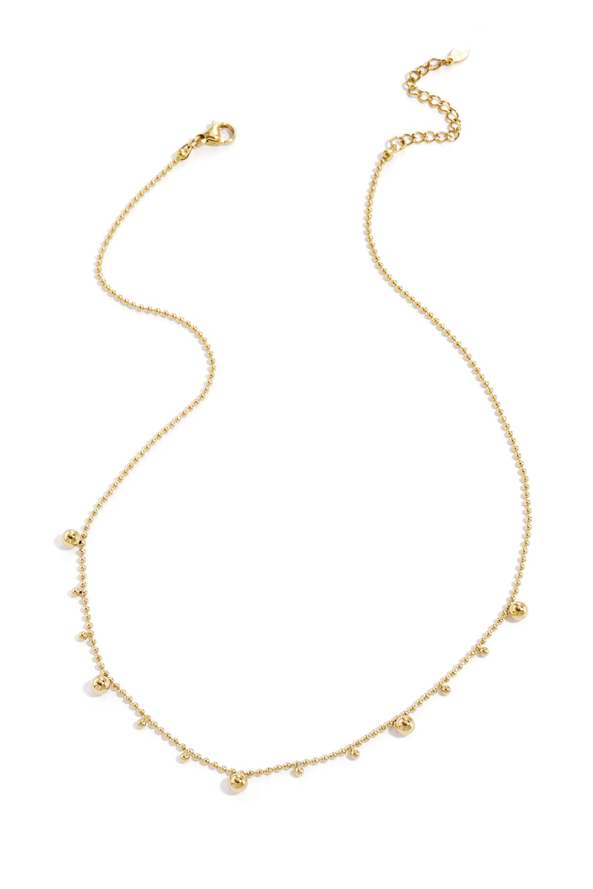 Gold tone delicate polka dot necklace with alternating small and larger beads laid flat on white background