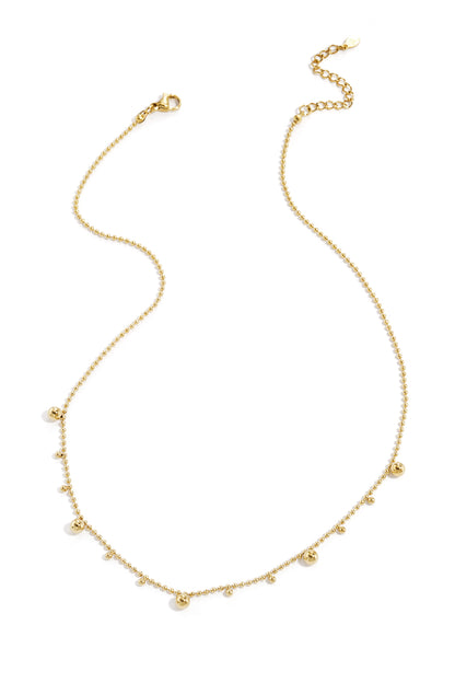 Gold tone delicate polka dot necklace with alternating small and larger beads laid flat on white background
