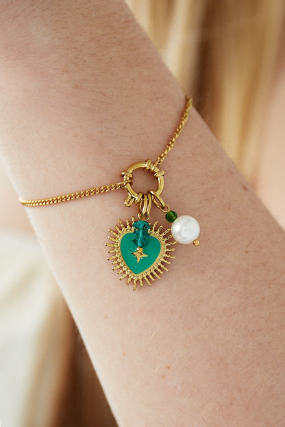Close-up of gold charm bracelet worn on wrist featuring green enamel heart, pearl, and teal bead charms