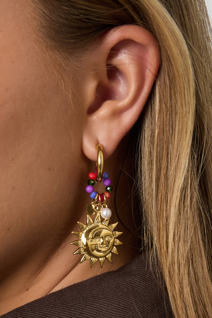 Close-up detailed shot of golden sun charm earring hanging from woman's ear, showing bright colorful beads and pearl detail