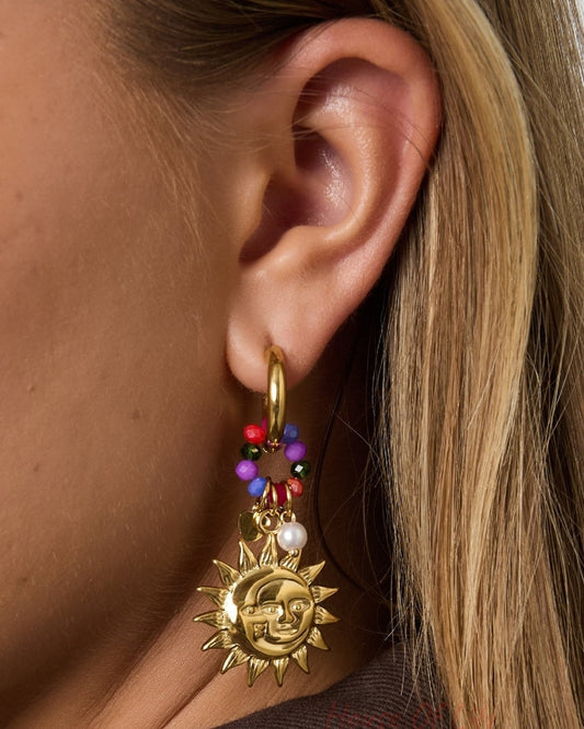 Close-up detailed shot of golden sun charm earring hanging from woman's ear, showing bright colorful beads and pearl detail