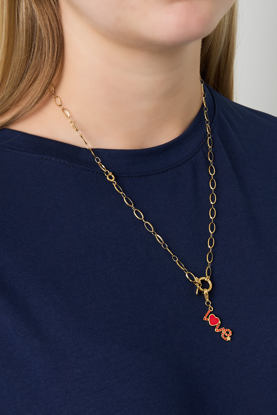 Model wearing gold link necklace with red 'LOVE' charm pendant over a navy blue top