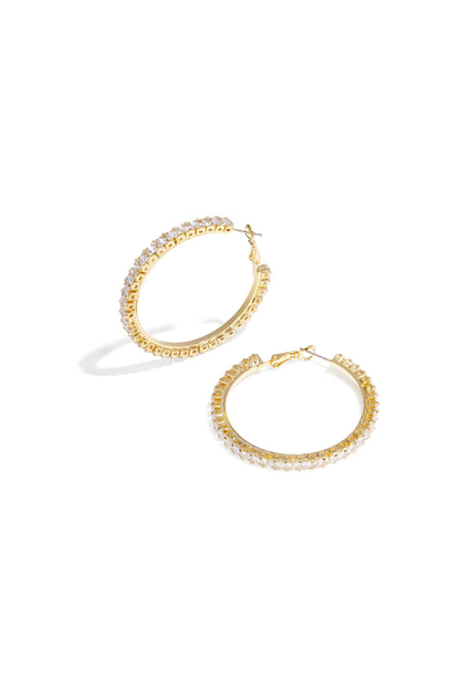 Close-up of gold-tone hoop earrings encrusted with clear crystals, displayed flat on a white background.