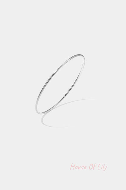 Thin minimalist silver bangle bracelet on white background with shadow