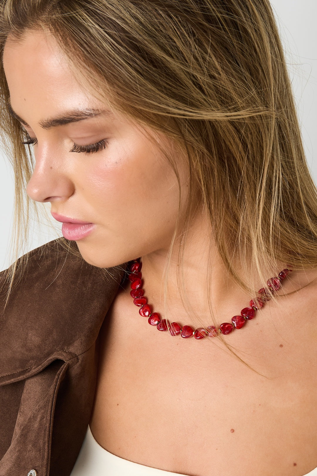 Close-up photo of a woman wearing the red heart-shaped acrylic beaded necklace paired with brown jacket and white top