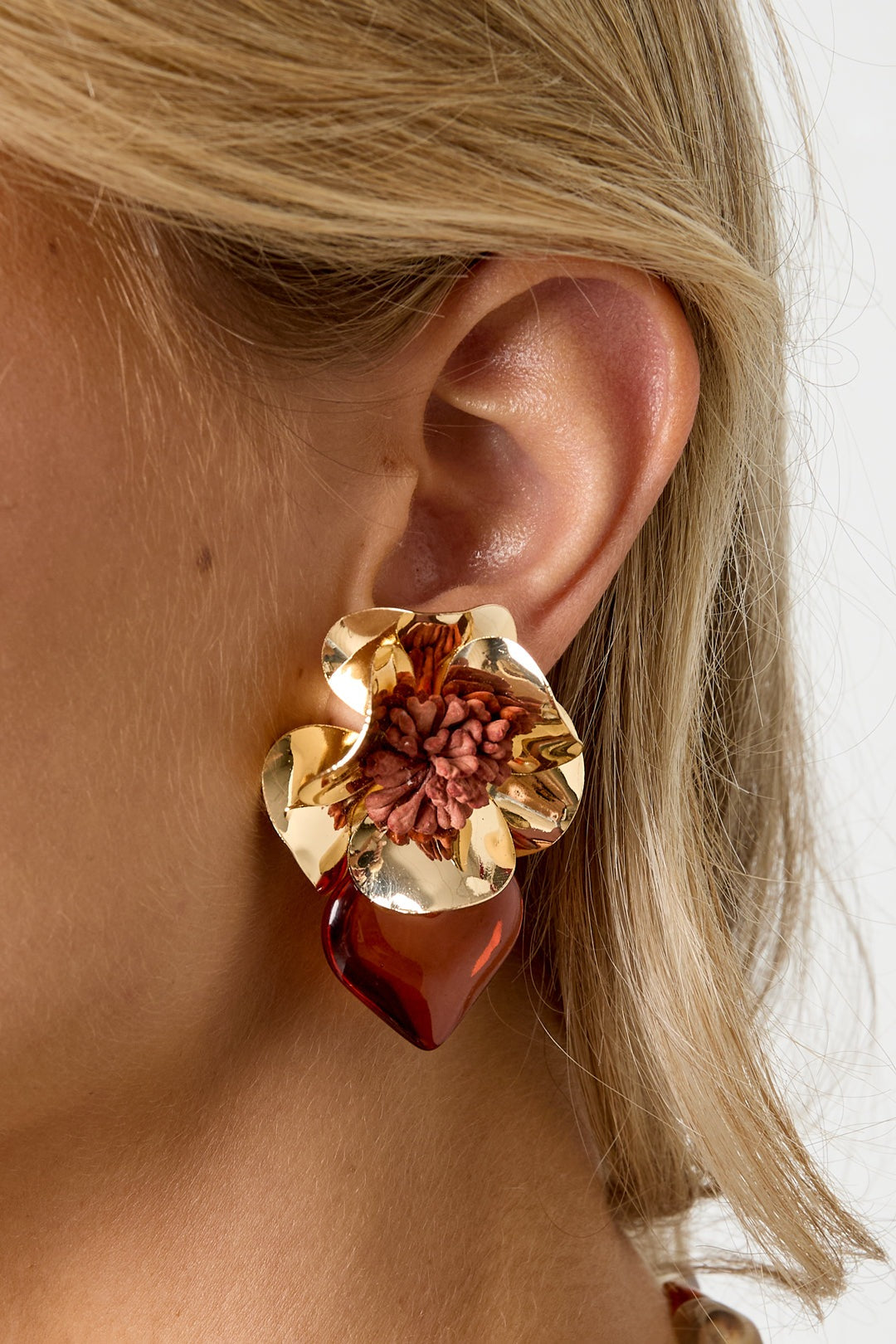 Close-up of model’s ear wearing warm brown floral heart drop earring with gold flower and resin heart