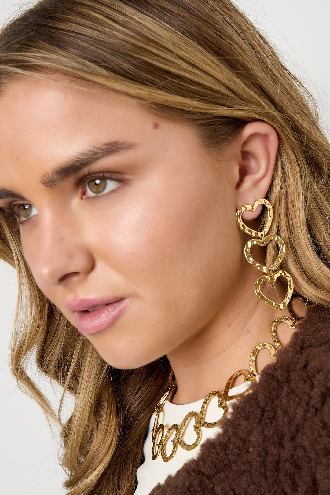 Close-up profile of woman wearing gold triple heart hammered dangle earrings and matching necklace