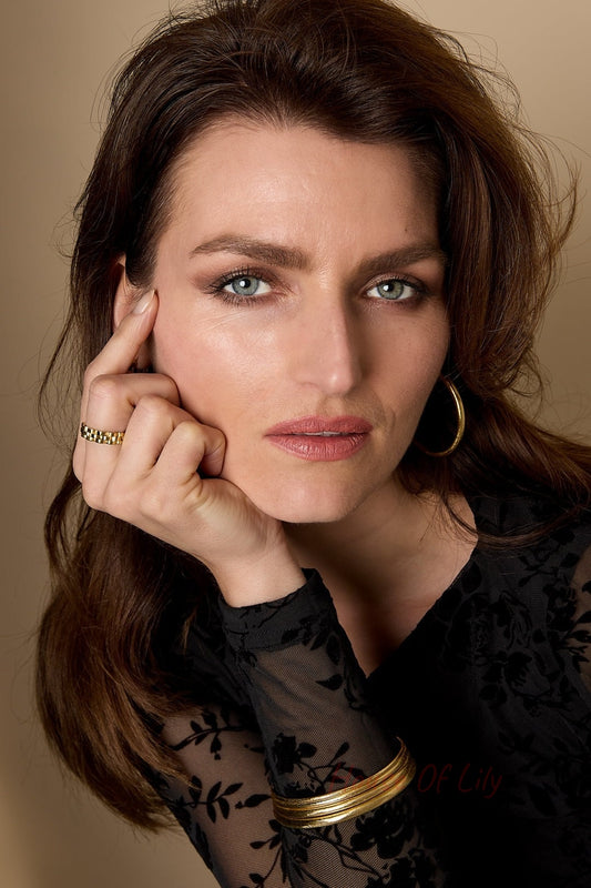 Woman wearing gold hoop earrings, a gold checkered ring and multiple gold bangles with sheer black floral top