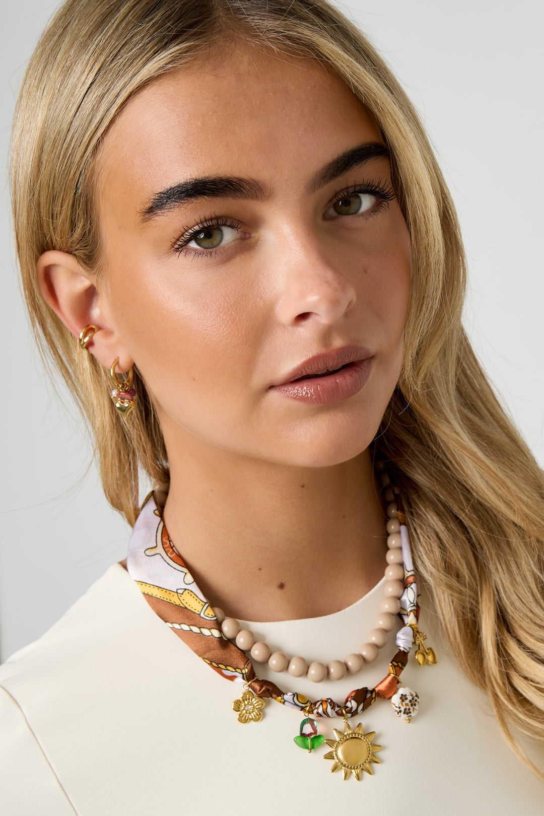 Blonde woman wearing the patterned fabric charm necklace paired with beaded necklace and gold earrings