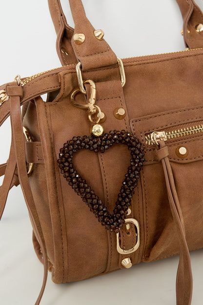 Brown beaded heart keychain attached to brown handbag with gold studs and zipper