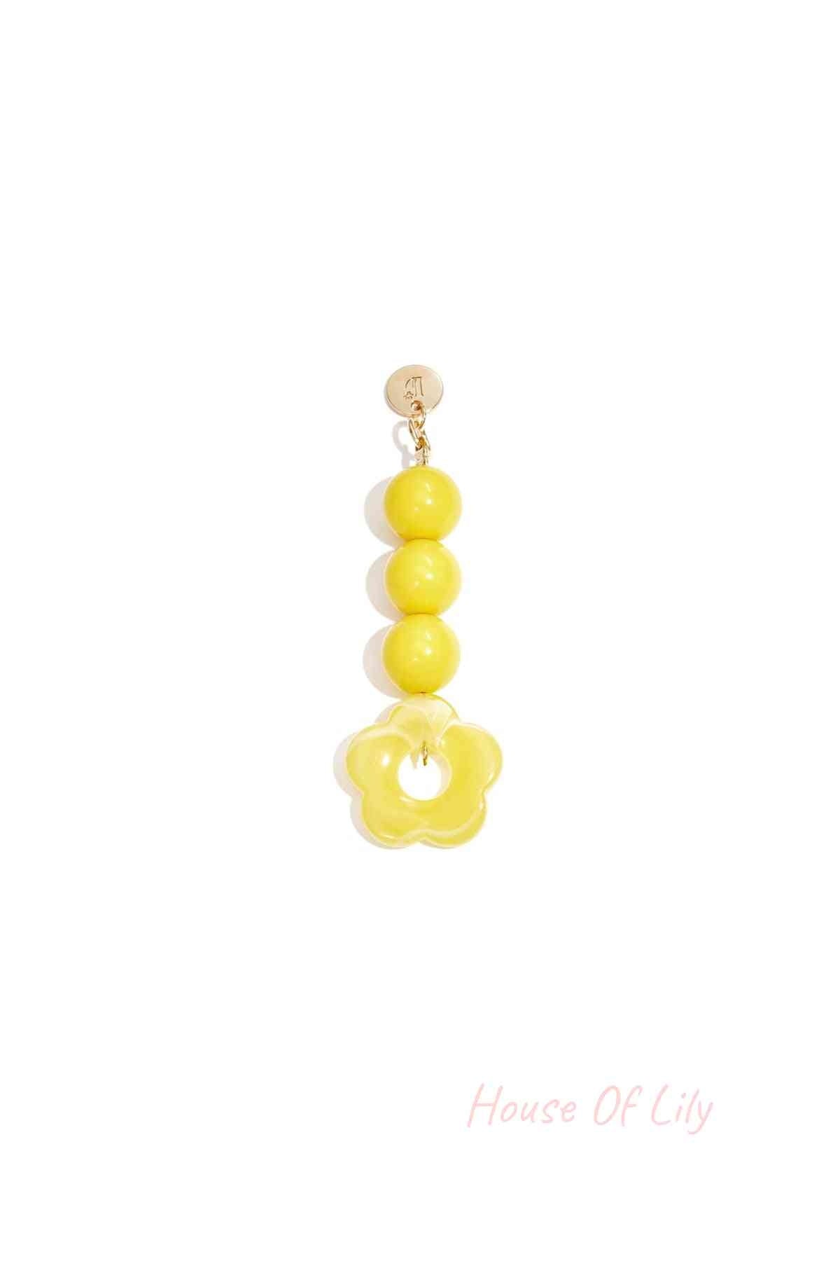 Yellow acrylic flower bag charm with three round yellow beads hanging from a gold clasp on white background