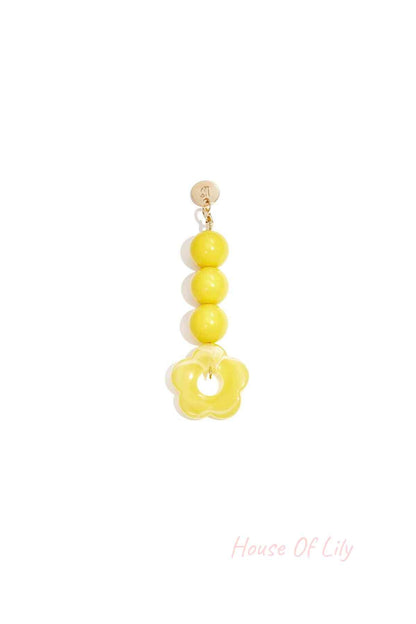 Yellow acrylic flower bag charm with three round yellow beads hanging from a gold clasp on white background