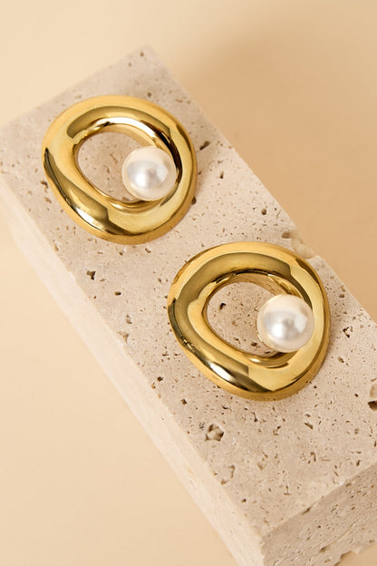 Pair of gold-tone circle pearl stud earrings displayed on textured beige stone block