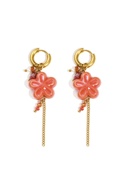 Pair of gold hoop drop earrings with coral resin flower pendants, decorated with faceted beads and delicate gold chain tassels on white background