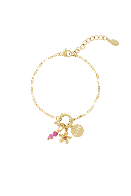 Gold charm bracelet worn with pink flower enamel charm, love disc, pink beads on white background