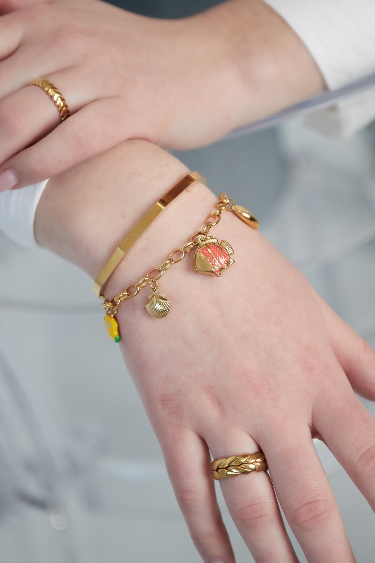 Close-up of bracelet worn on wrist paired with gold rings, showing detailed sea-inspired charms