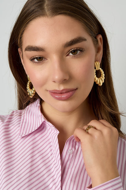 Model wearing twisted gold hoop earrings and matching ring while dressed in a pink striped shirt