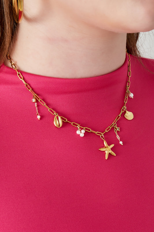 Close-up of woman wearing the gold seaside charm necklace styled with a bright pink top