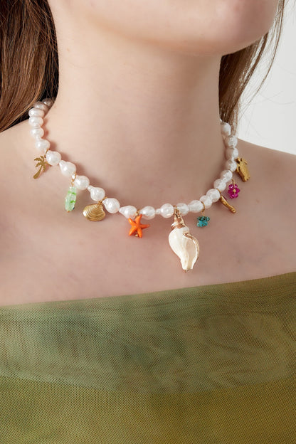 Model wearing the pearl necklace with ocean charms, showcasing clavicle-length fit and vibrant details against a skin tone and green off-shoulder top