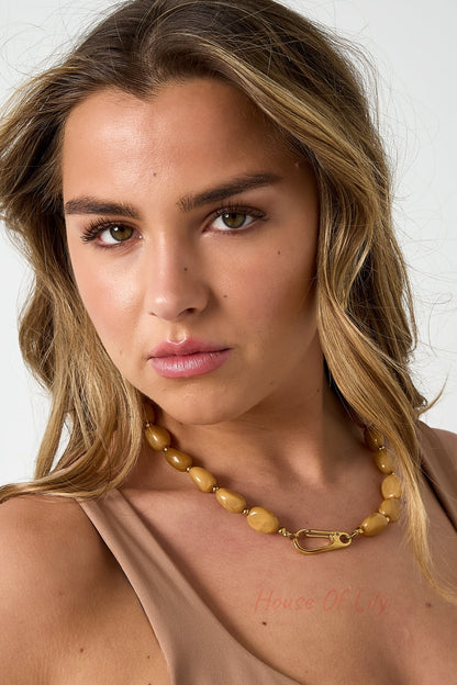 Woman wearing a mustard acrylic beaded necklace with gold-tone clasp paired with a nude tank top