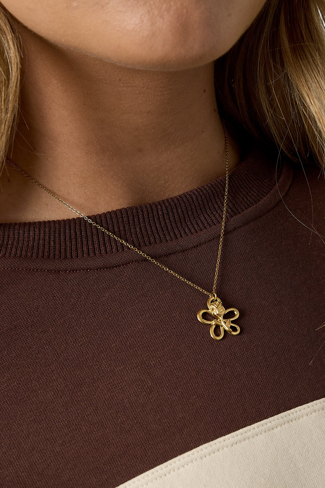 Close-up front detail of youthful woman wearing gold floral pendant necklace with sculptural flower on delicate chain