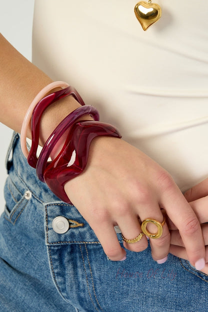 Model wearing four acrylic bangles in red, purple, pink, and marbled colors, paired with gold rings and denim jeans