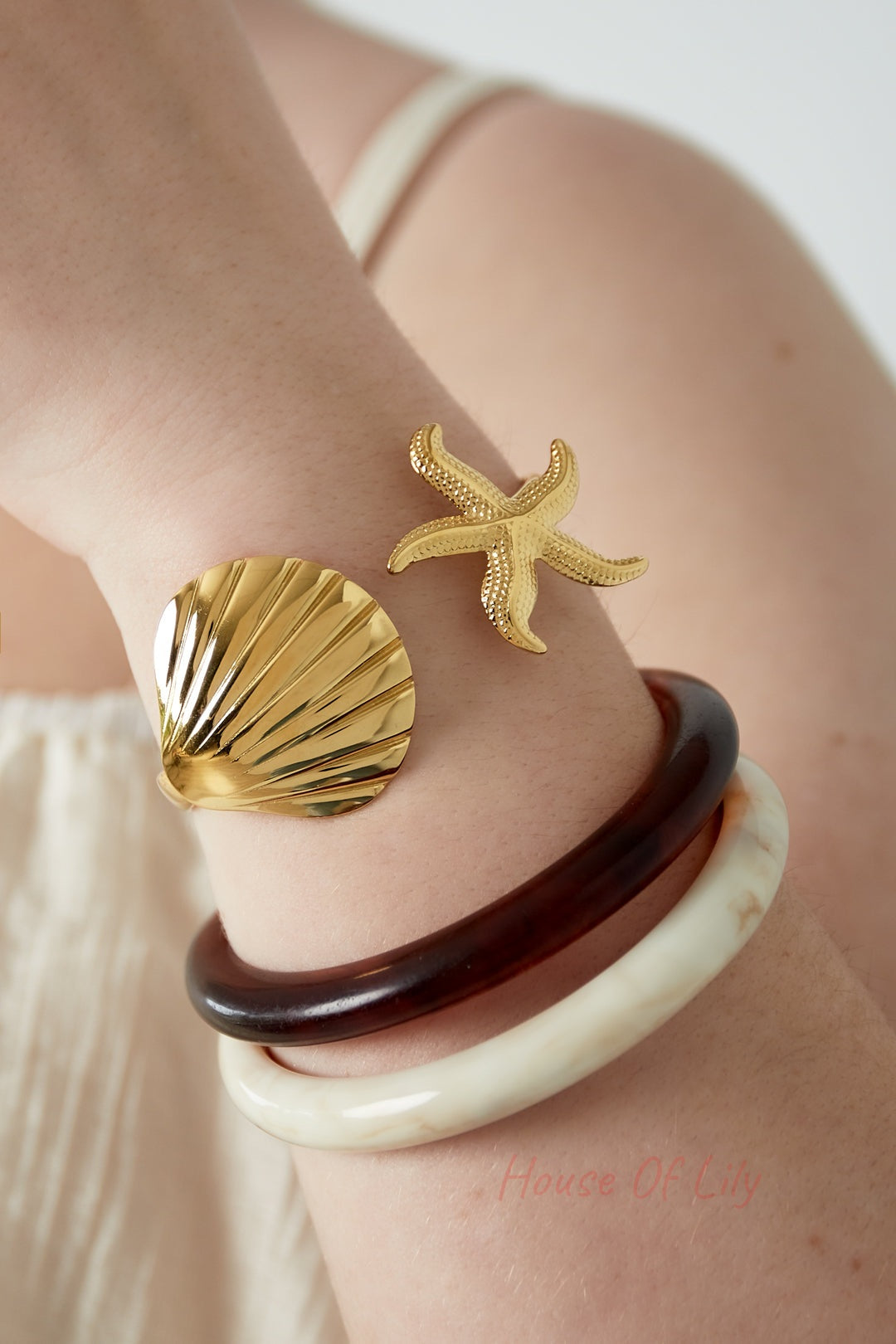 Close-up of a woman's wrist wearing the gold shell and starfish bangle along with two resin bangles, capturing a youthful and boutique style look
