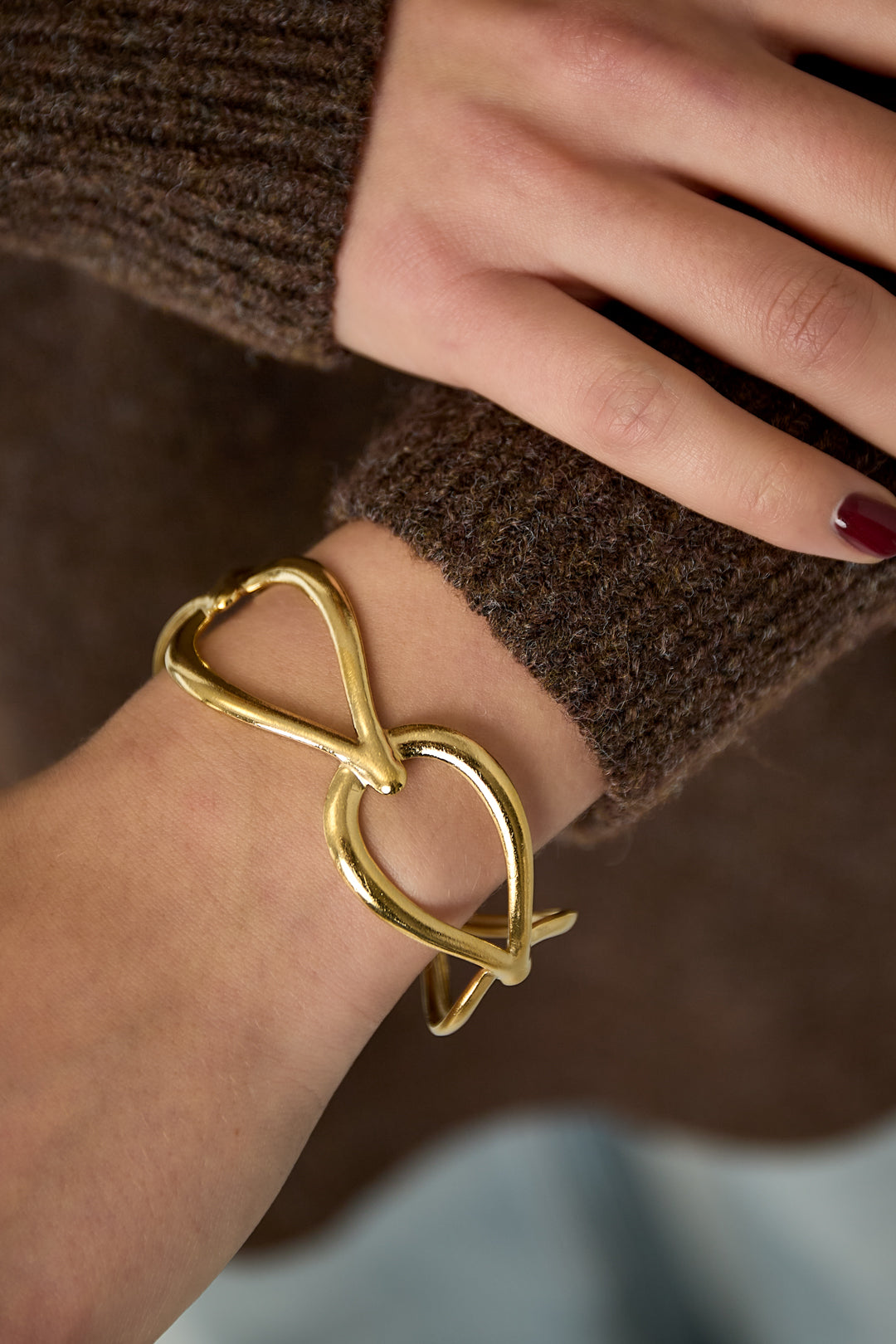 Close-up of woman wearing gold open loop cuff bracelet on wrist with brown knit sweater