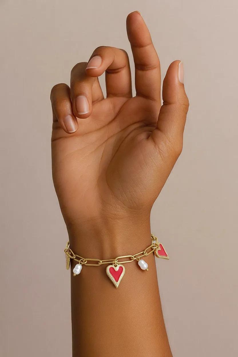 Gold-tone link chain bracelet featuring enamel red heart charms and dangling white pearls on a wrist.