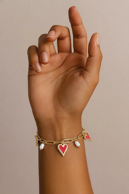 Gold-tone link chain bracelet featuring enamel red heart charms and dangling white pearls on a wrist.