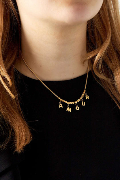 Close-up of woman wearing gold Amour pendant necklace over black top highlighting necklace detail
