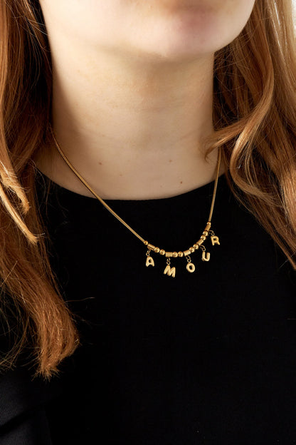 Close-up of woman wearing gold Amour pendant necklace over black top highlighting necklace detail