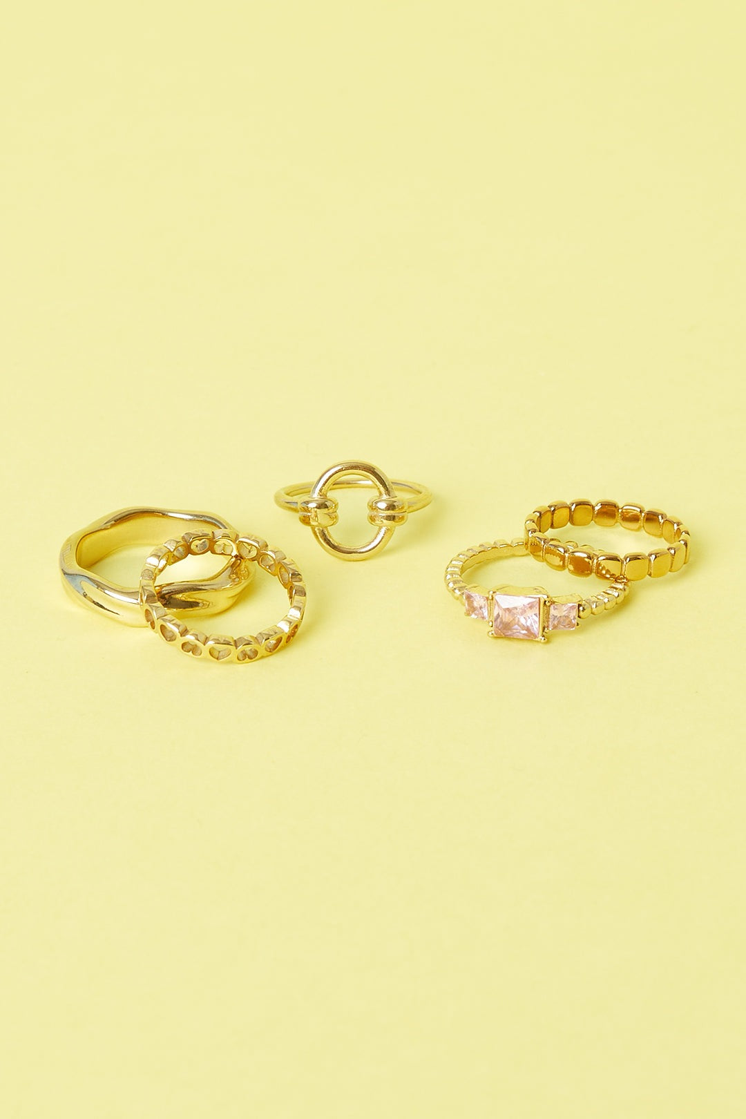 Group of four gold rings including a circle knot ring on yellow background