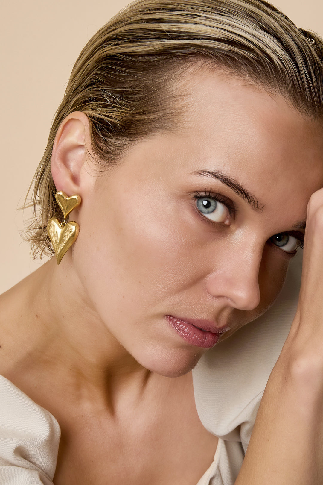Close-up side view of a woman wearing gold heart drop earrings, showcasing their size and playful design