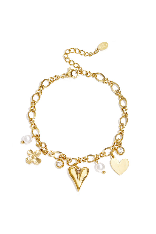 Gold charm bracelet featuring chain links with heart, flower, rhinestone and pearl charms laid flat on white background