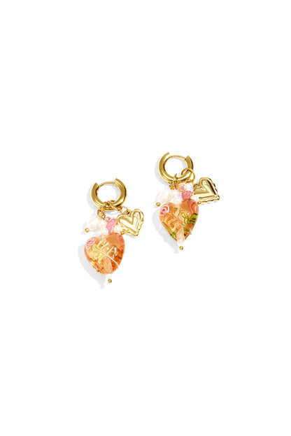 Pair of gold hoop earrings with peach-colored heart charms decorated with floral details, pearl accents, and gold mini hearts on white background