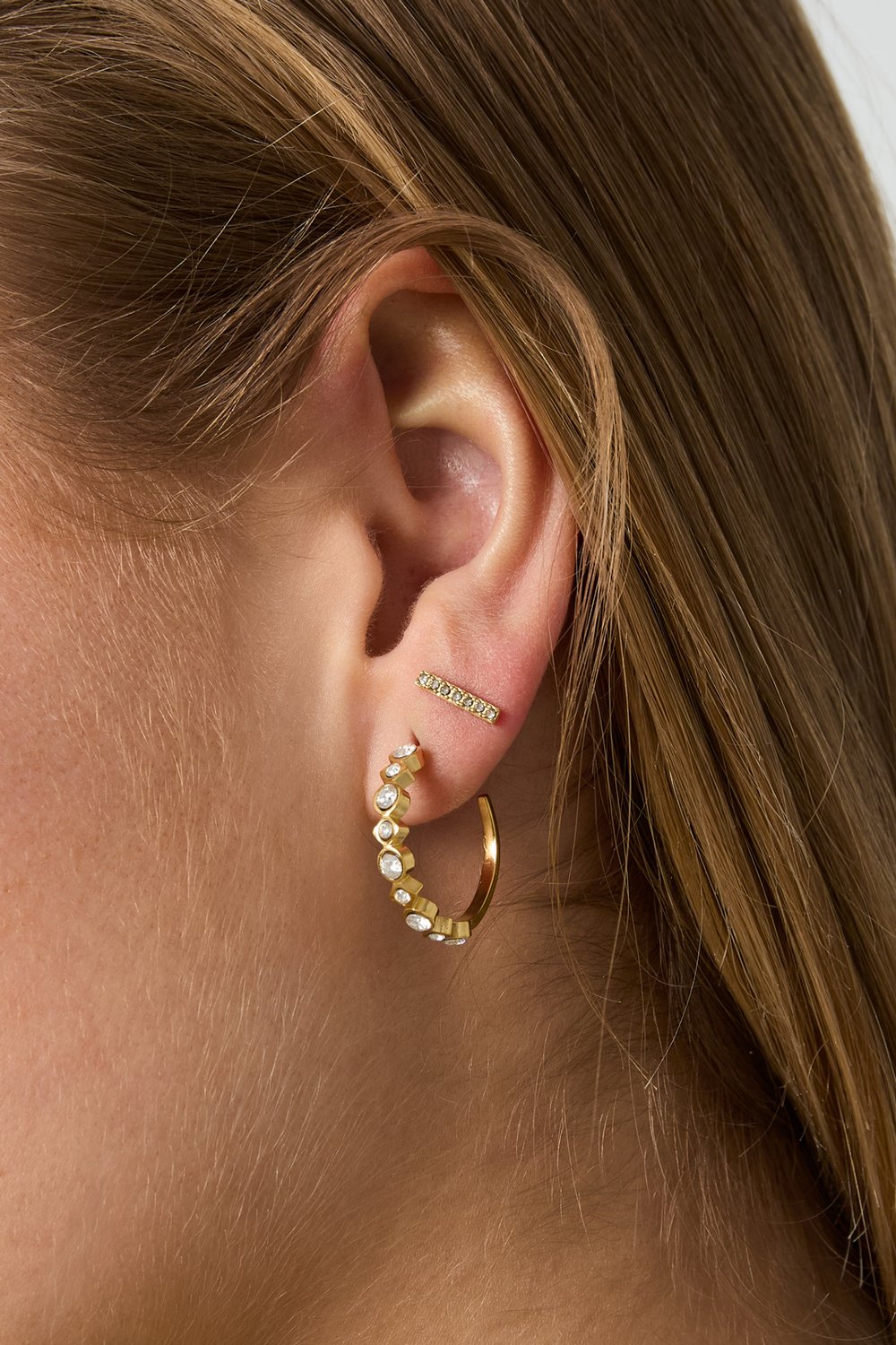 Glitch Beam Studs: Gold bar earring with embedded crystals worn on an earlobe alongside a crystal-studded gold hoop.