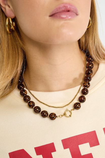 Close-up of model’s neck showcasing the leopard print acrylic beaded necklace alongside a delicate gold chain necklace