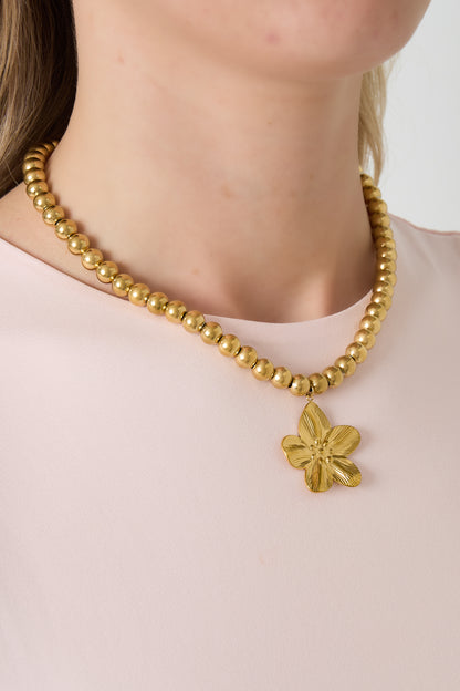 Model wearing gold beaded necklace with flower pendant paired with light pink top