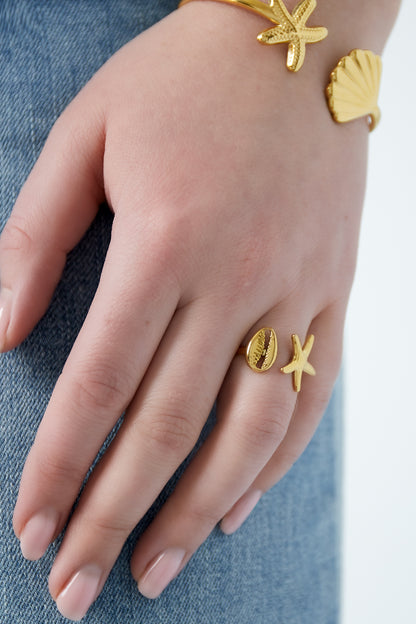 Close-up of hand wearing a gold-tone starfish and seashell open ring with blue denim background
