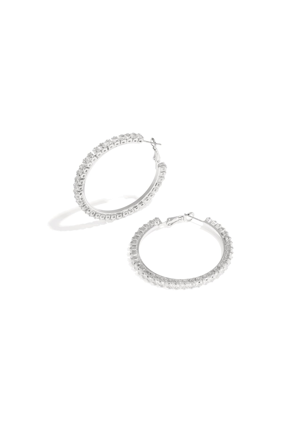 Close-up of silver-tone crystal-encrusted hoop earrings lying flat on a white background.