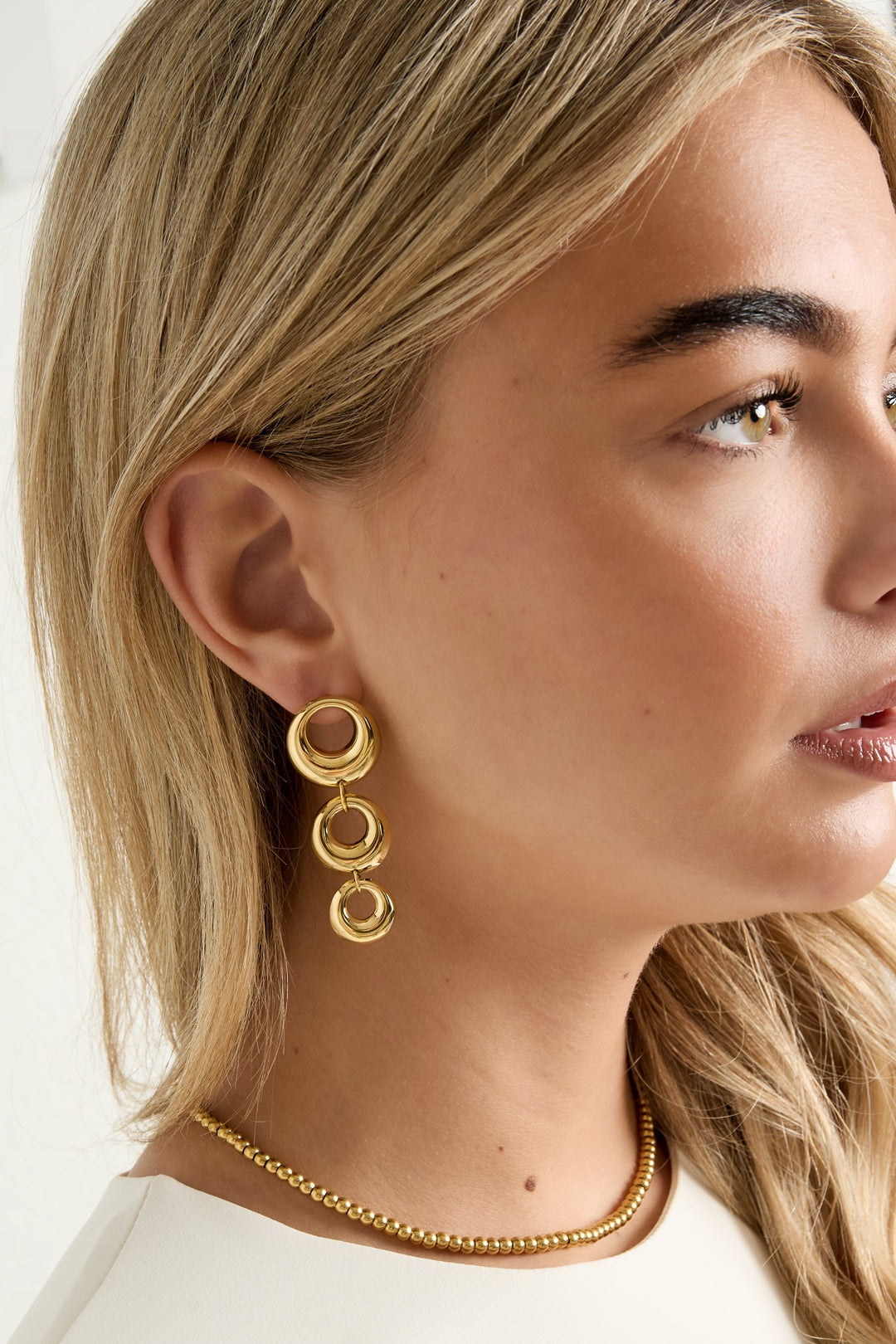 Side profile of woman wearing chunky linked circle gold dangle earrings showcasing length and design