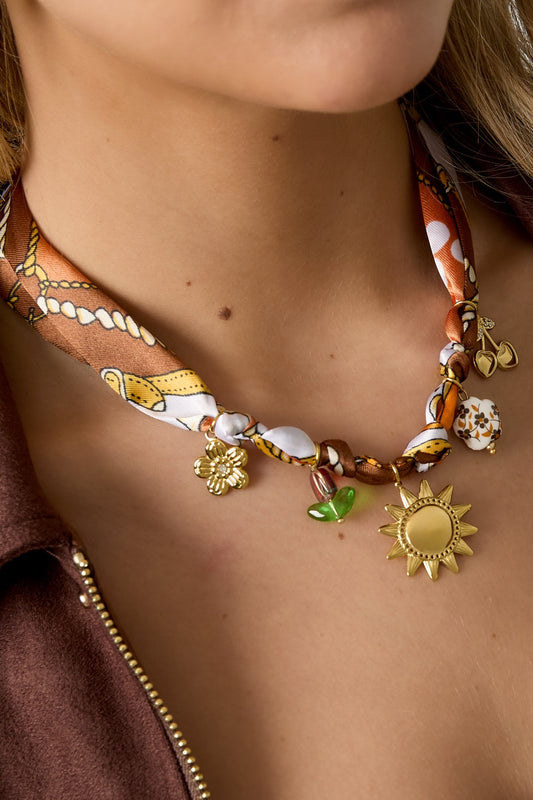 Close-up of the patterned fabric charm necklace with playful gold charms worn on model’s neck