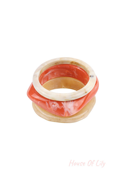 Set of three resin bangles stacked showing colors orange, beige, and blue with a marbled finish from a top angle
